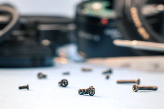 Scattered screws on a white surface with blurred tools, ideal for repair themes. How to Find a Phone Repair Shop That Actually Uses OEM Parts