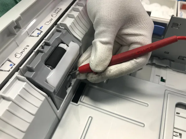 A gloved hand fixes a printer using a red precision tool, showcasing maintenance skills. Checklist for a used printer or scanner: page counts, drums, and ports
