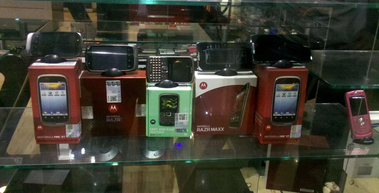 Older Motorola phones and boxes displayed behind glass in a store